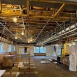 Lane Road's interior with suspended ceiling framework, temporary lighting, and scaffolding in large open room.