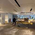 The Lane Road library 1st floor with drywall ceiling, exposed wiring, scaffolding, and a worker near stair railing.